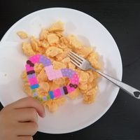 Hand holding a plate of cereal with a beaded heart on top