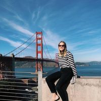 Woman in a striped top sitting on a wall in front of the Golden Gate Bridge