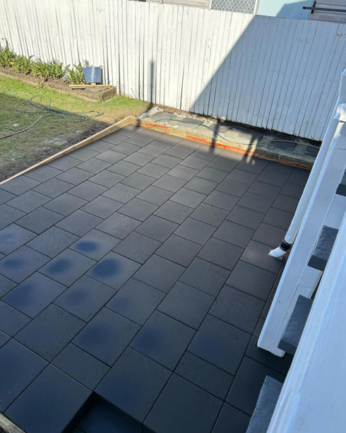 Dark grey square pavers laid beside white timber stairs and a fence