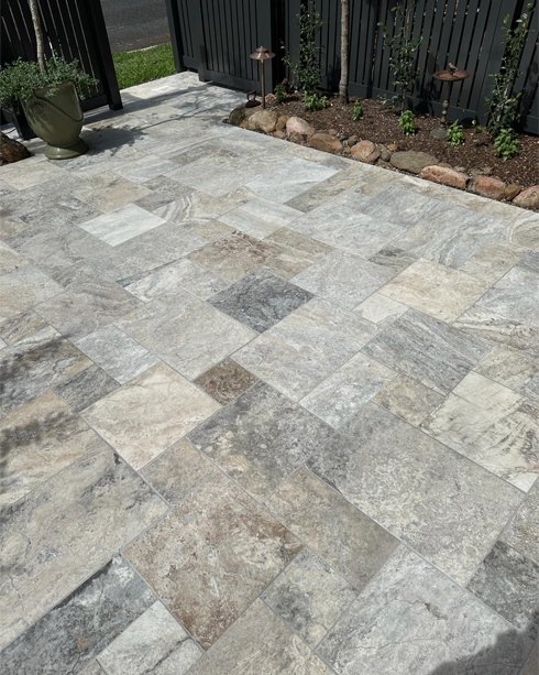 Grey and cream stone-look pavers in a courtyard beside a black fence and garden bed