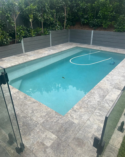 Rectangular pool with grey paved surrounds and glass pool fencing