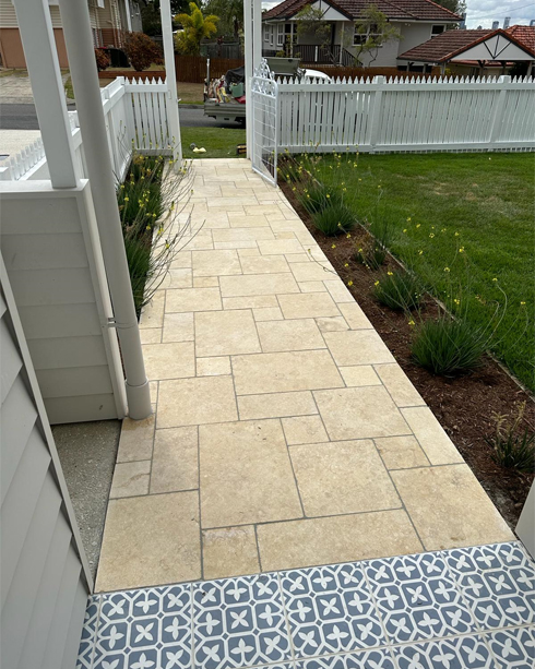 Beige paved path beside a verandah, with a strip of patterned tiles at the front