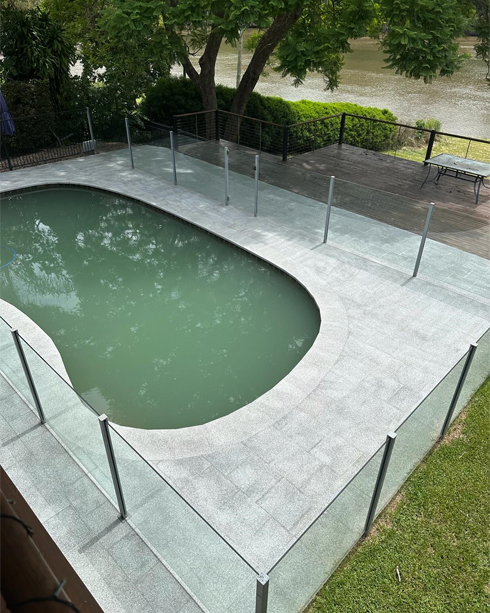 Kidney-shaped pool with light grey paved surrounds and a glass pool fence